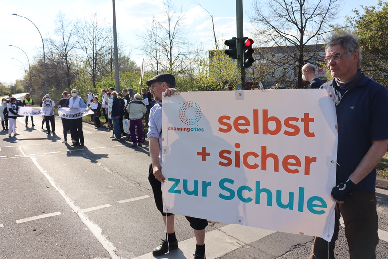 Demonstrationsteilnehmende zeigen Banner und Schilder: selbst + sicher zur Schule