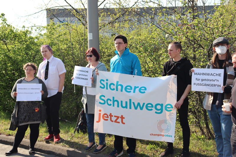 Demonstrationsteilnehmende zeigen Banner und Schilder: Sichere Schulwege jetzt